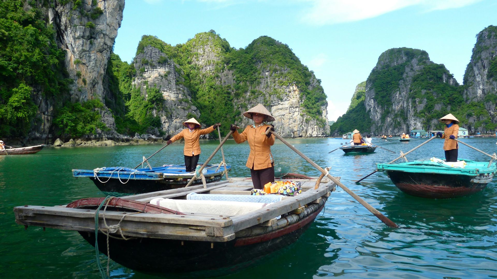 A woman in a conical hat rowing a boat between the green islands of Hạ Long Bay