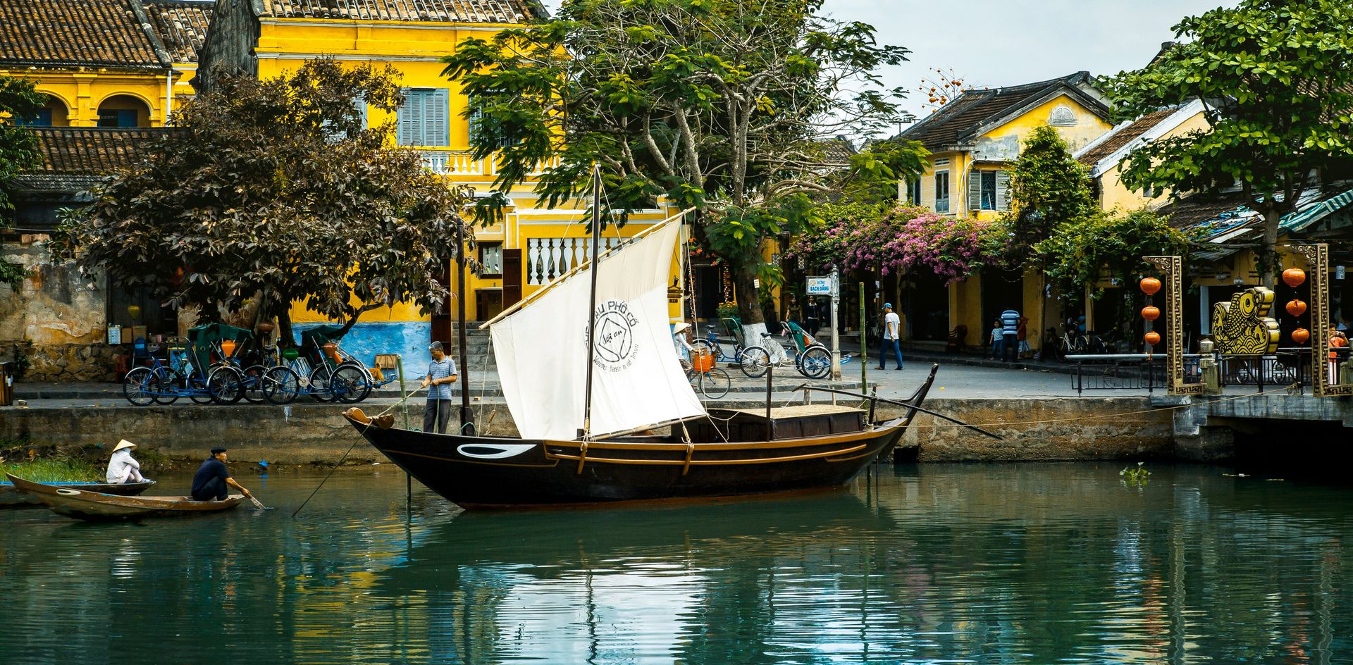 A wooden boat with a white sail moored on the river in Hội An