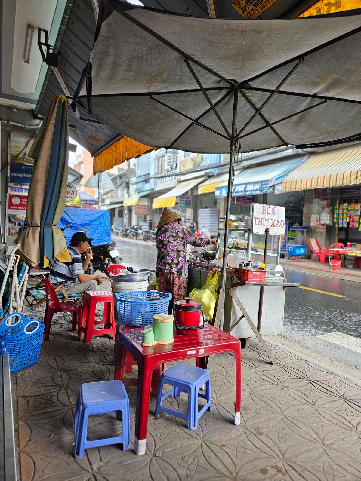 A street food stall with small red plastic stools on a Vietnamese sidewalk